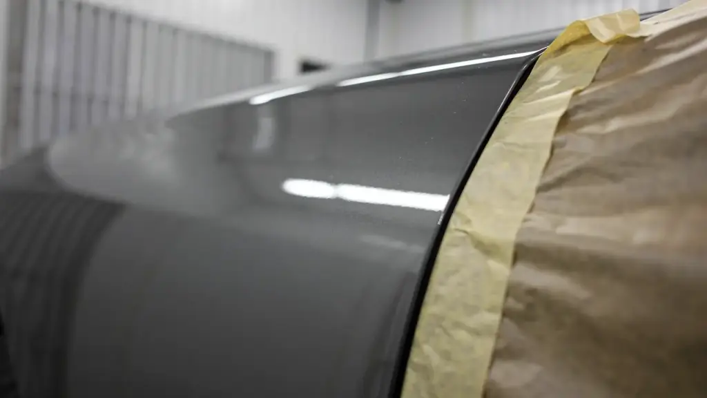 Freshly cleared body panel beside masking paper and tape under spray-booth light